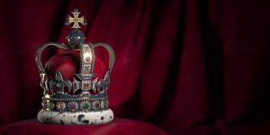 Royal golden crown with jewels on pillow on pink red background.